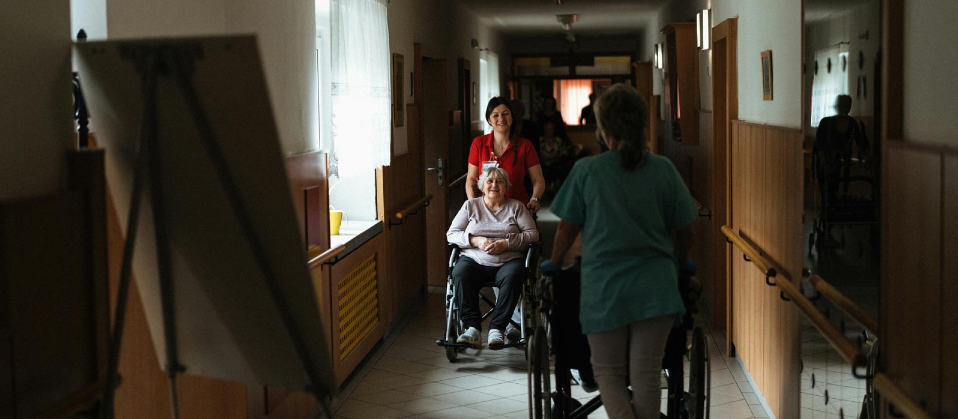 Residents in wheelchairs pushed by aides in the hallway