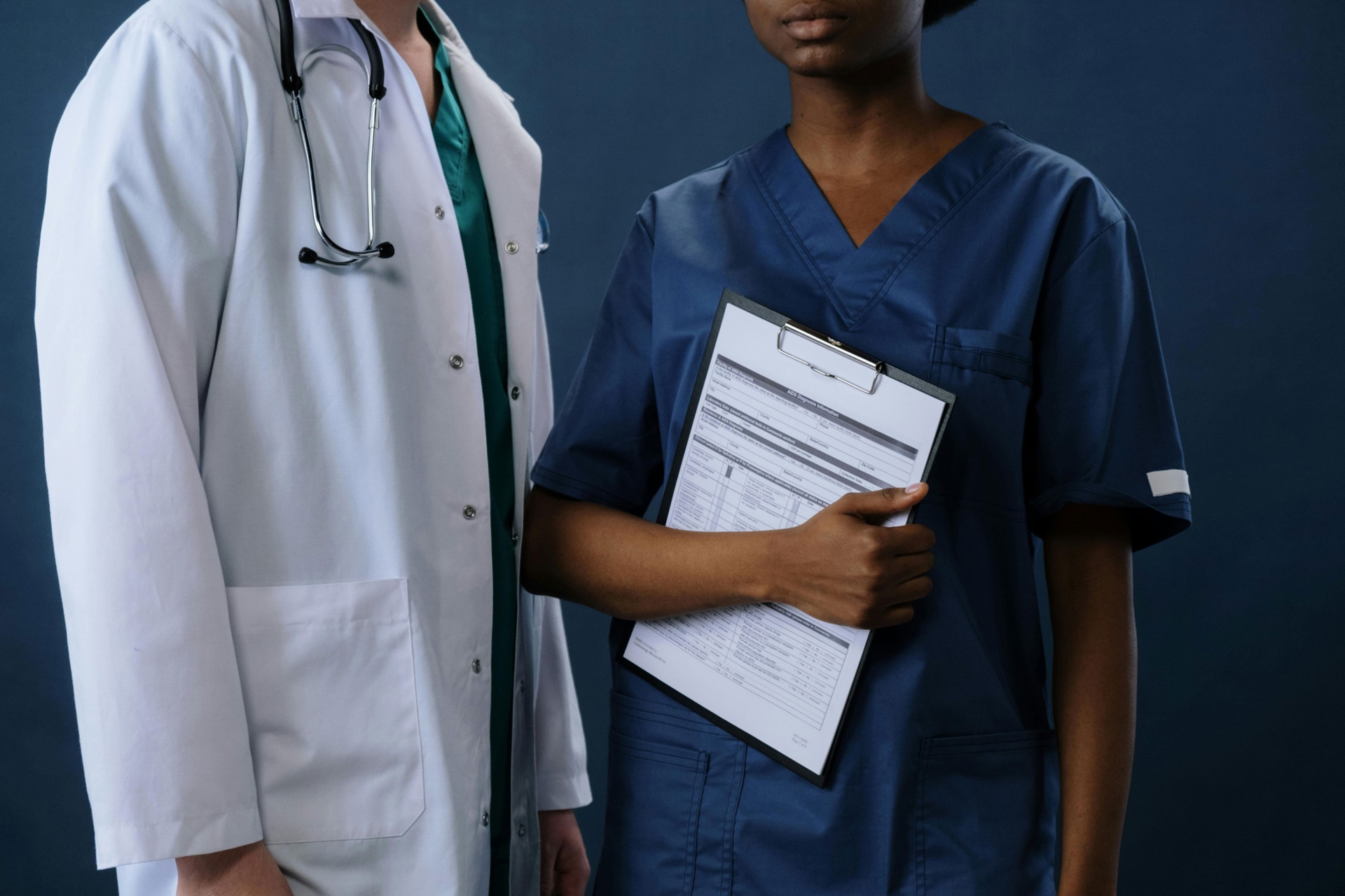 doctor in coat and nurse in scrubs with clipboard